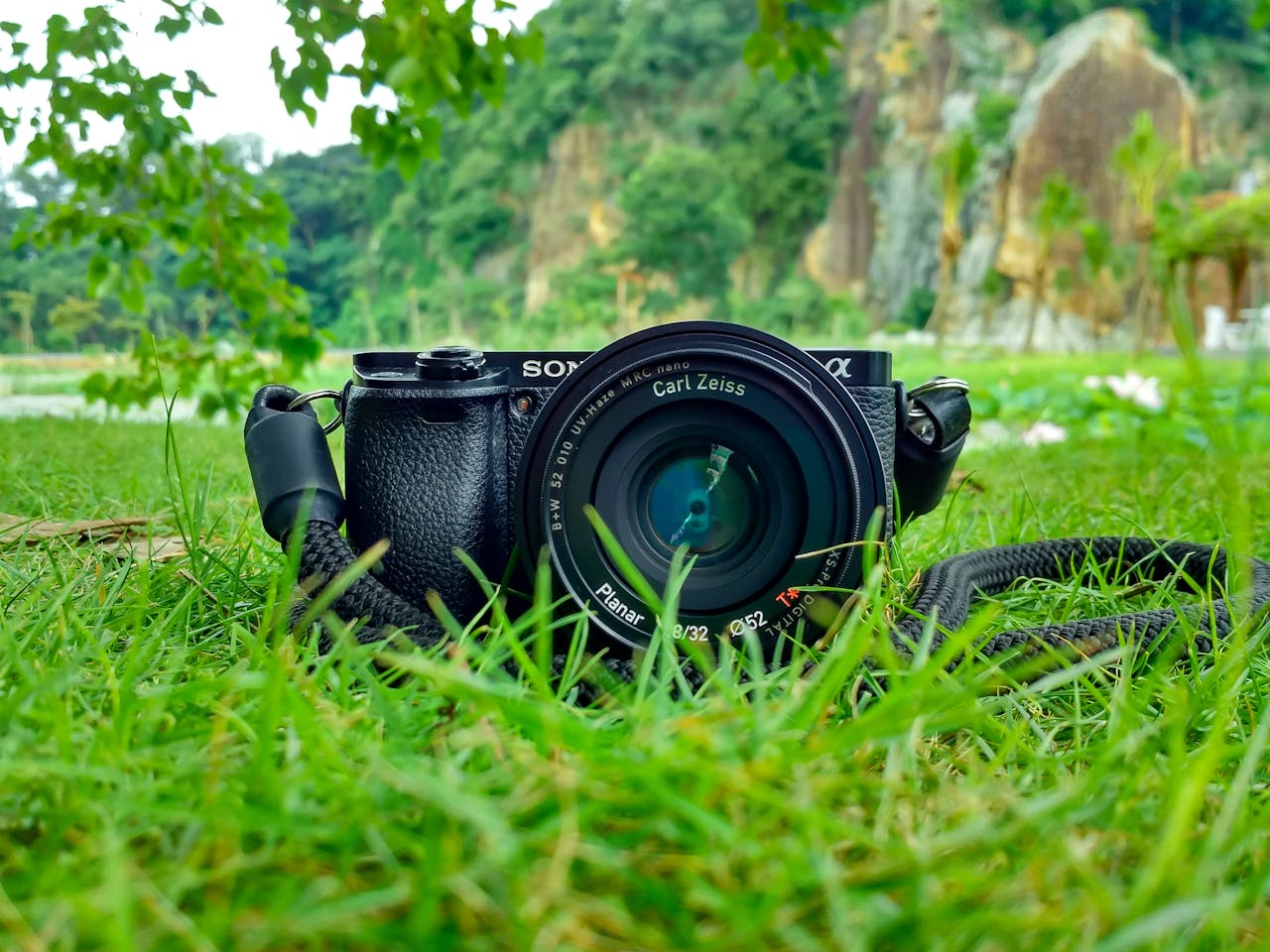 about-us-01 Camera with Carl Zeiss lens on grass, surrounded by nature and vibrant greenery.